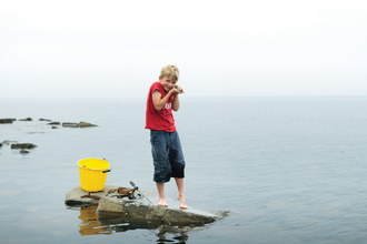 Archie stands on a rock in the sea with a bucket